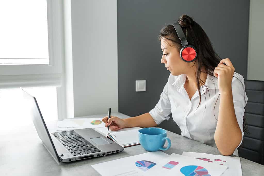young successful woman works using laptop and headphones. paper work. finance and planning.